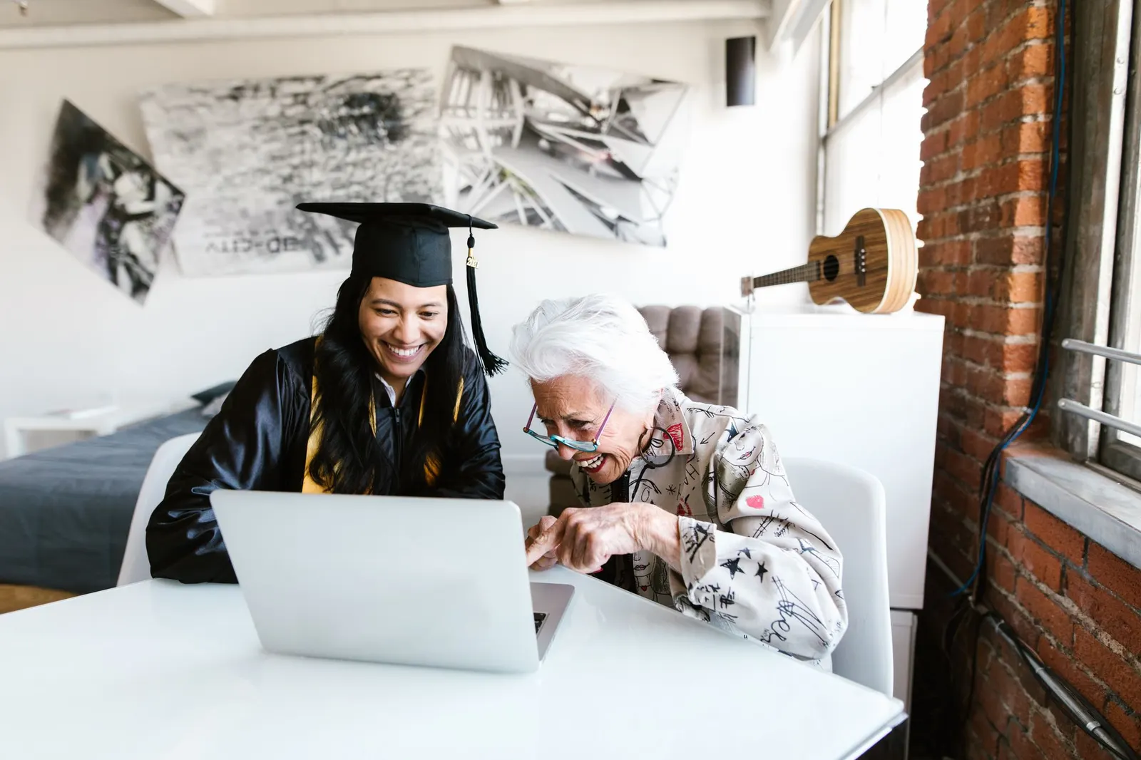 New AI degree graduate in cap and gown sharing a laptop screen with an older woman