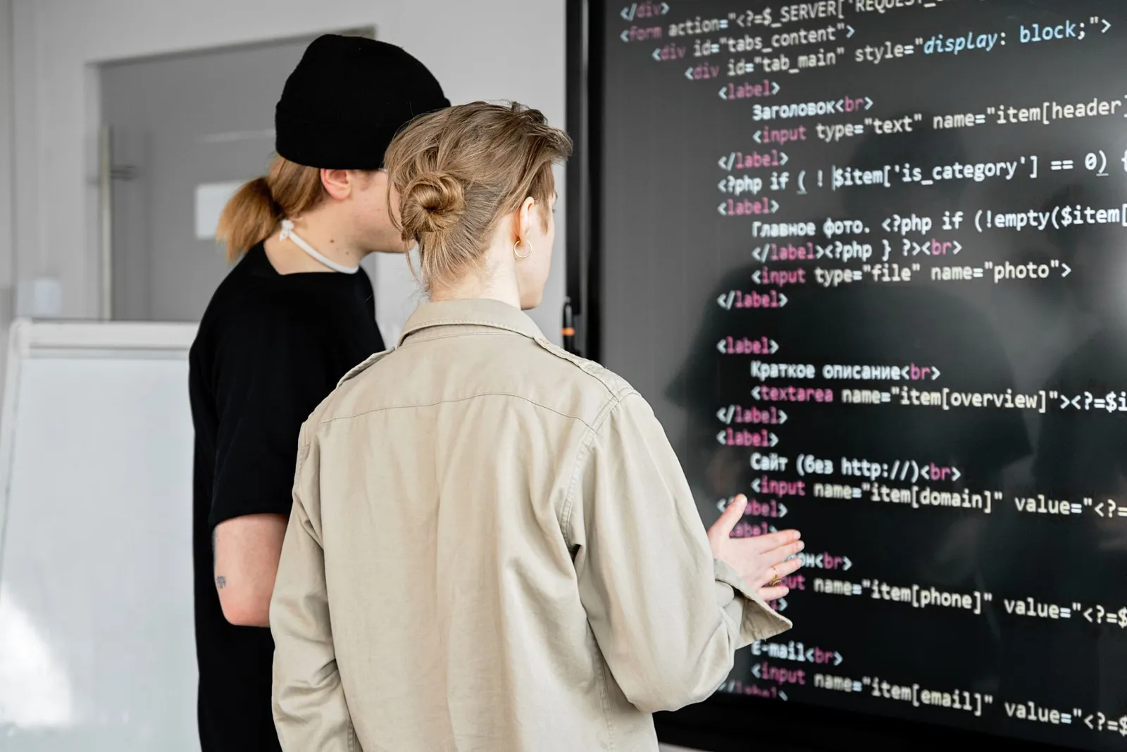 Two people discussing lines of code on a large wall screen, comparing an AI degree and a computer science degree