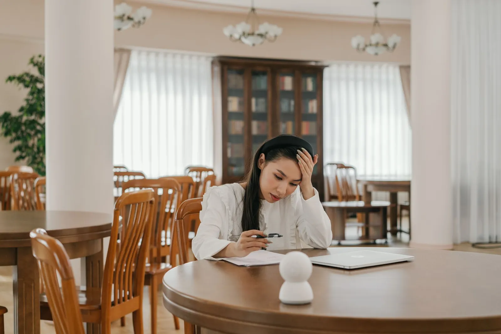 Woman studying papers at a library table with a laptop, exploring an AI degree for non-programmers