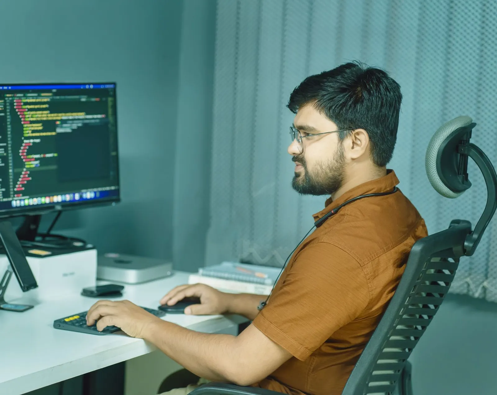 AI engineer in glasses writing code at a desk with a large monitor in a home office