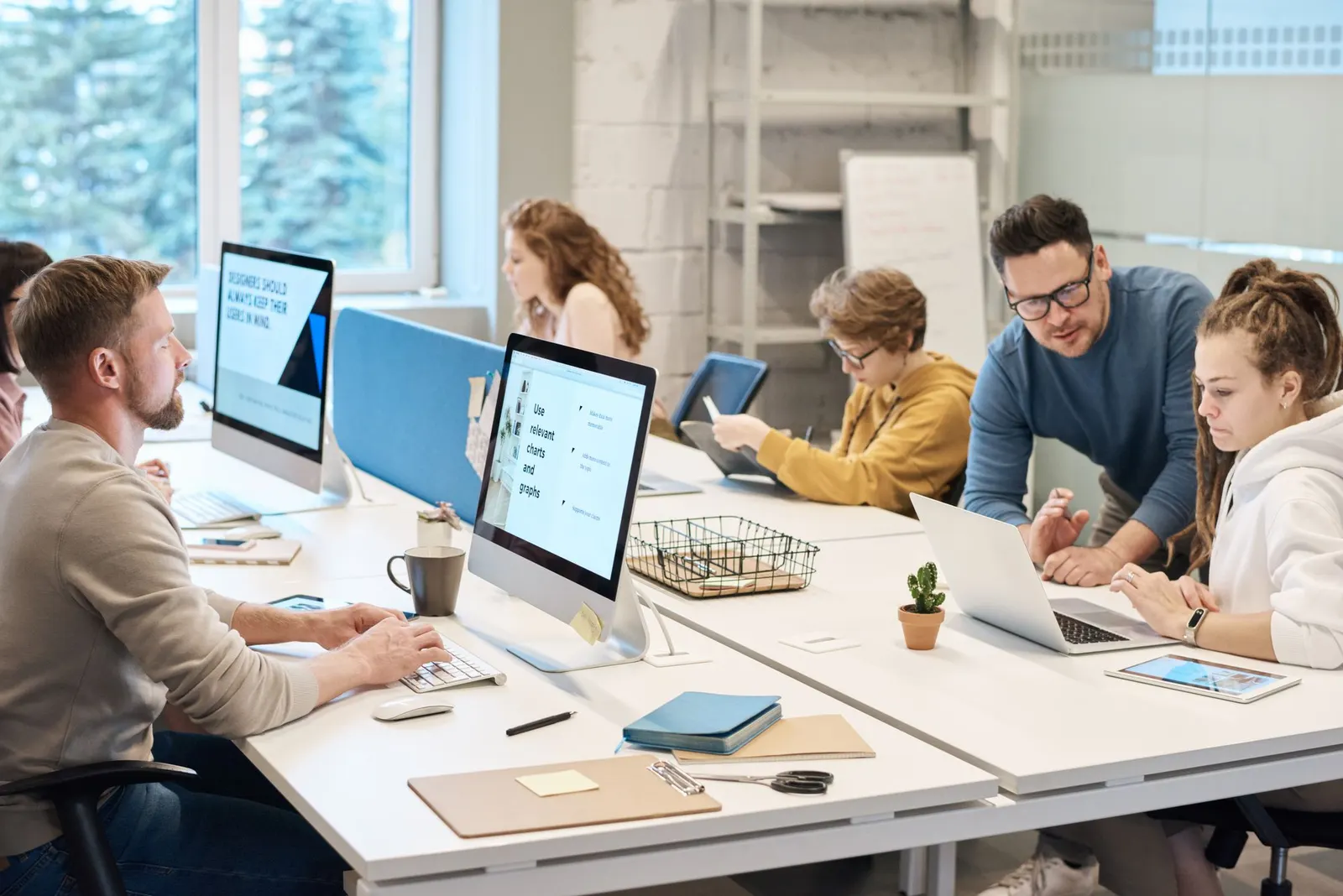 Coworkers in AI jobs at shared desks as one leans in to help a colleague