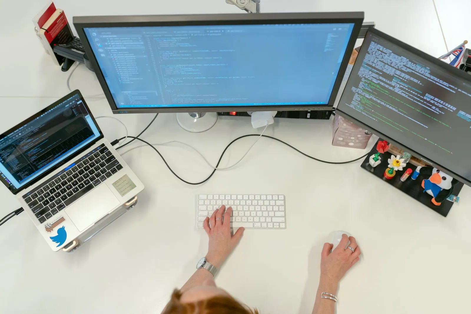 AI research scientist typing at a white desk with code on a laptop and two monitors