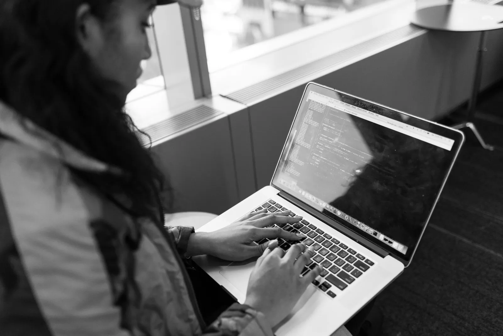 Woman typing code on a laptop by a window while studying for the AWS Certified AI Practitioner exam
