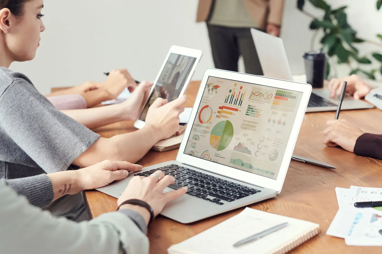 Business intelligence analysts around a team table reviewing charts on a laptop and tablet