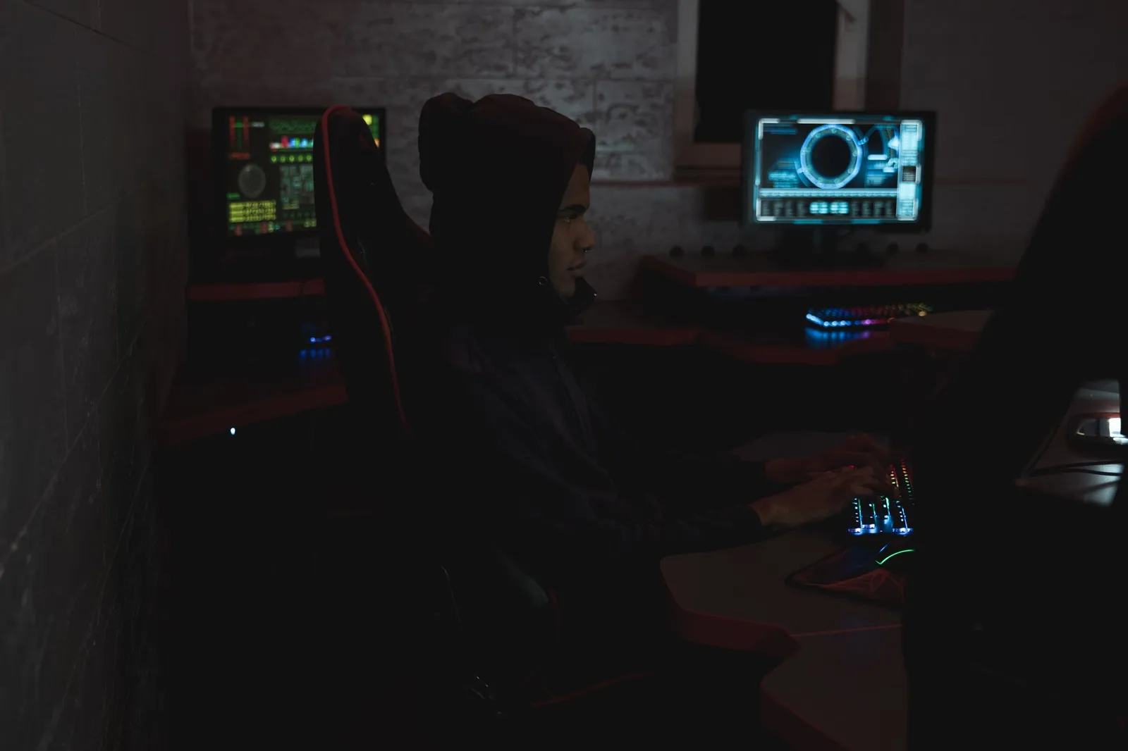 Person in a dark hoodie typing in a dim room with monitors glowing, studying for CompTIA AI certification