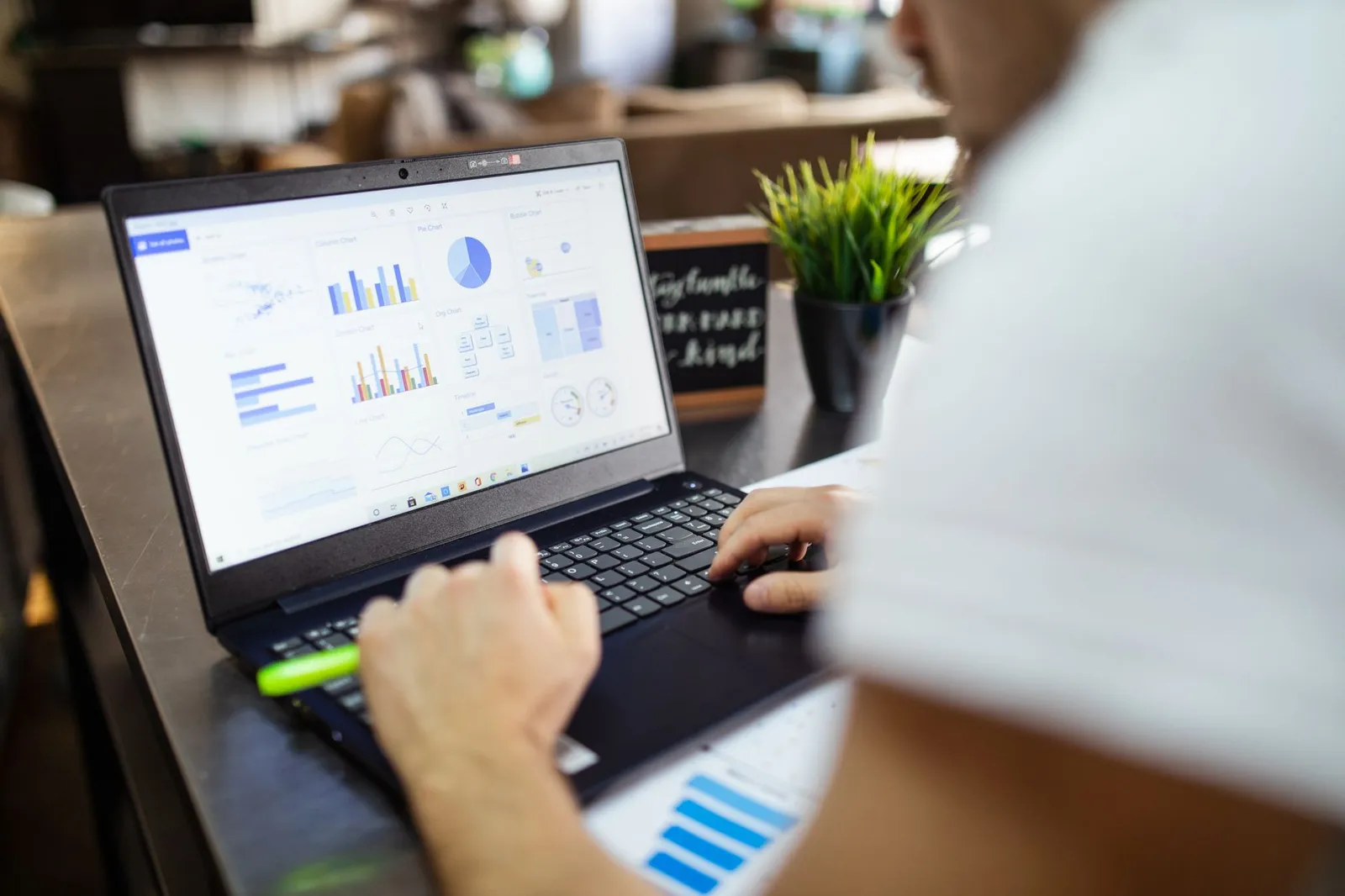 Data analyst typing on a laptop that shows a dashboard of bar, pie and line charts
