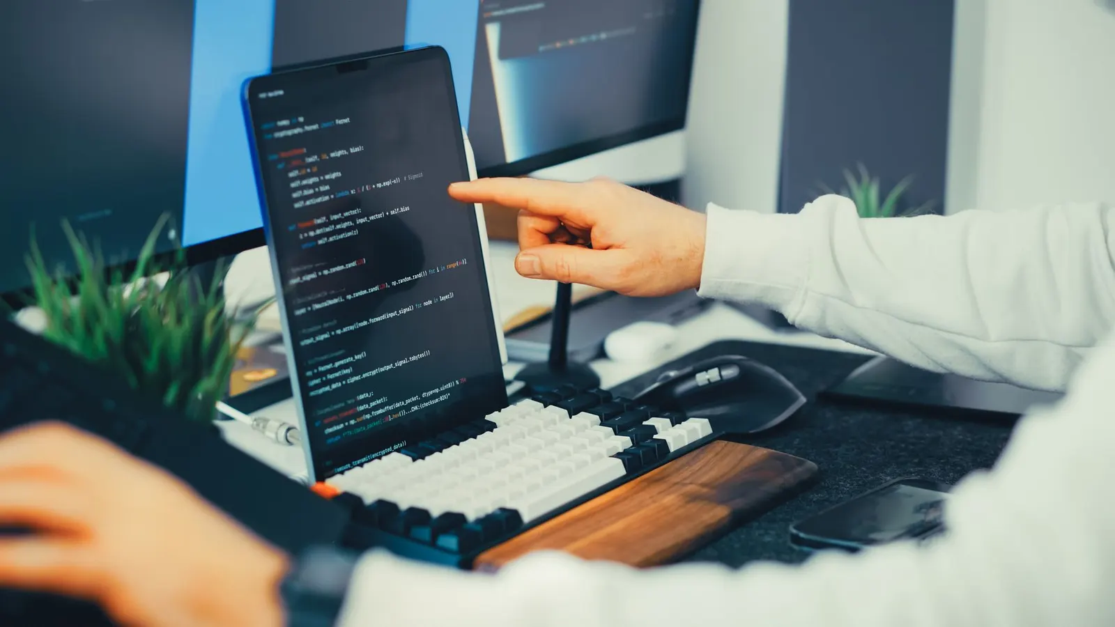 Data engineer pointing at Python code on a tablet at a desk with two monitors