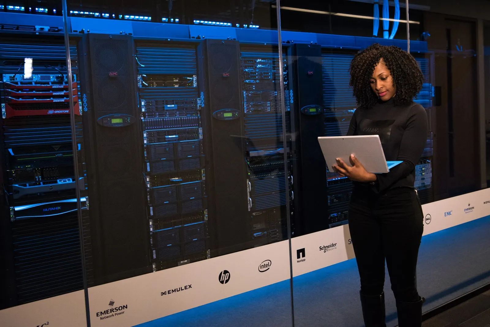 Data engineer holding a laptop in front of a glass wall of server racks