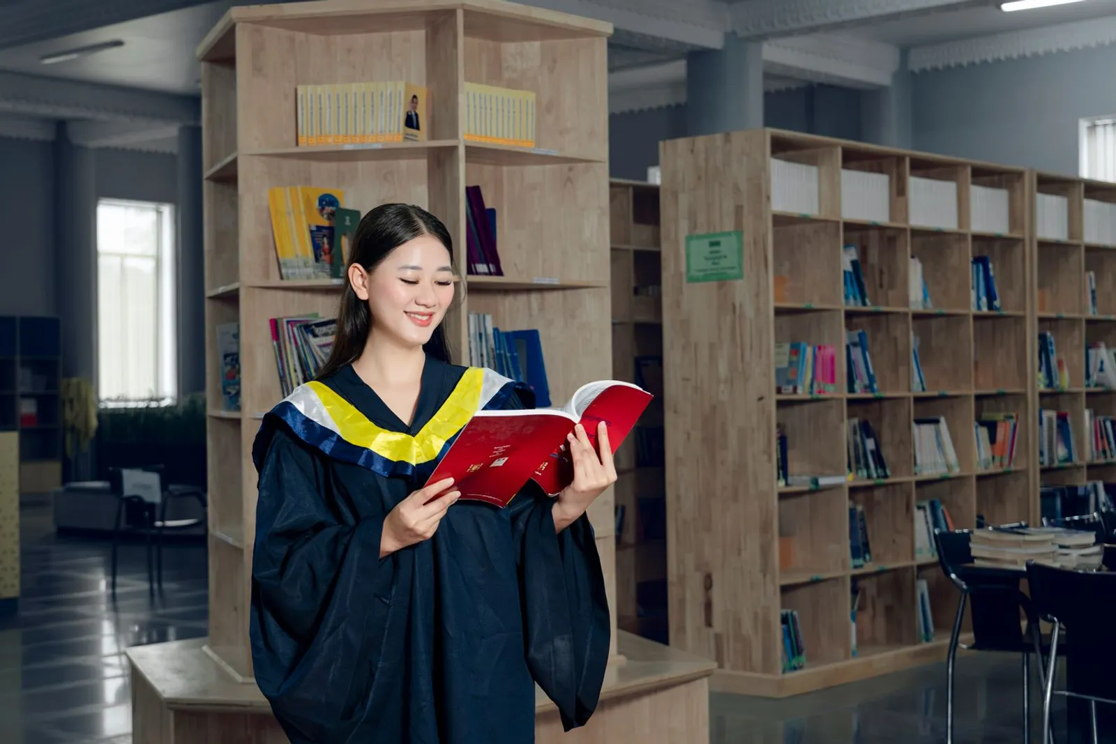 Woman in a graduation gown reading in a library, pursuing a graduate certificate in artificial intelligence