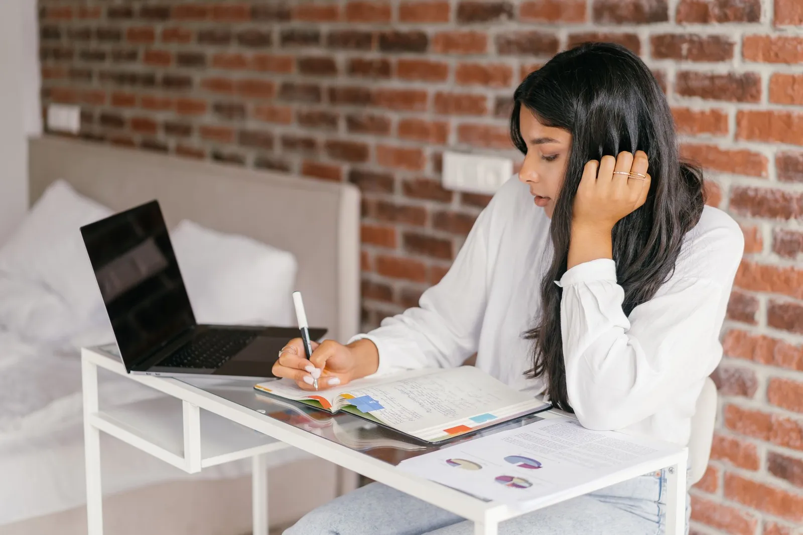 Student taking notes at a desk with a laptop while researching online AI degree guides