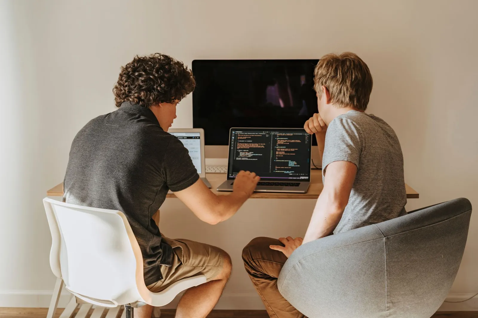 Two young men at a desk reviewing code on a laptop, learning how to become an AI engineer