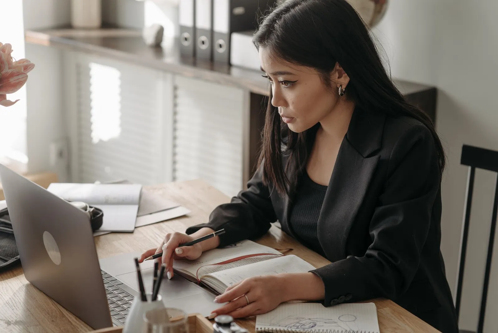 Woman taking notes beside a laptop at a home desk, studying for IBM AI engineering professional certificate