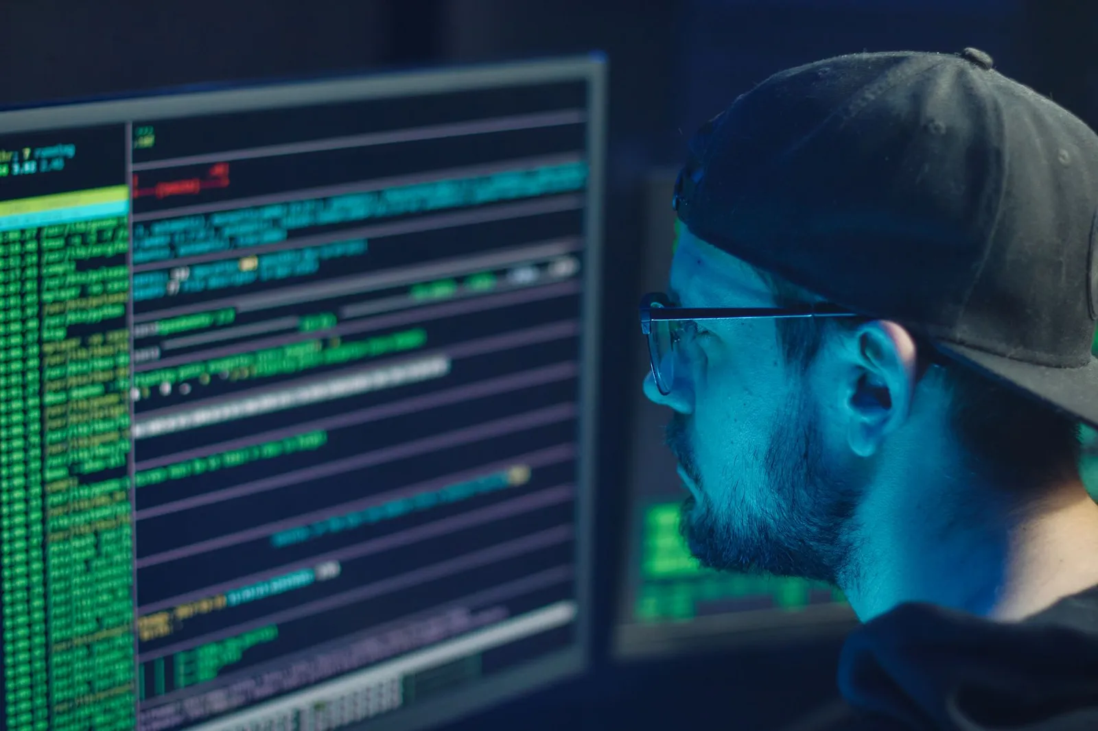 Information security analyst reading log output on a monitor in a dim blue room