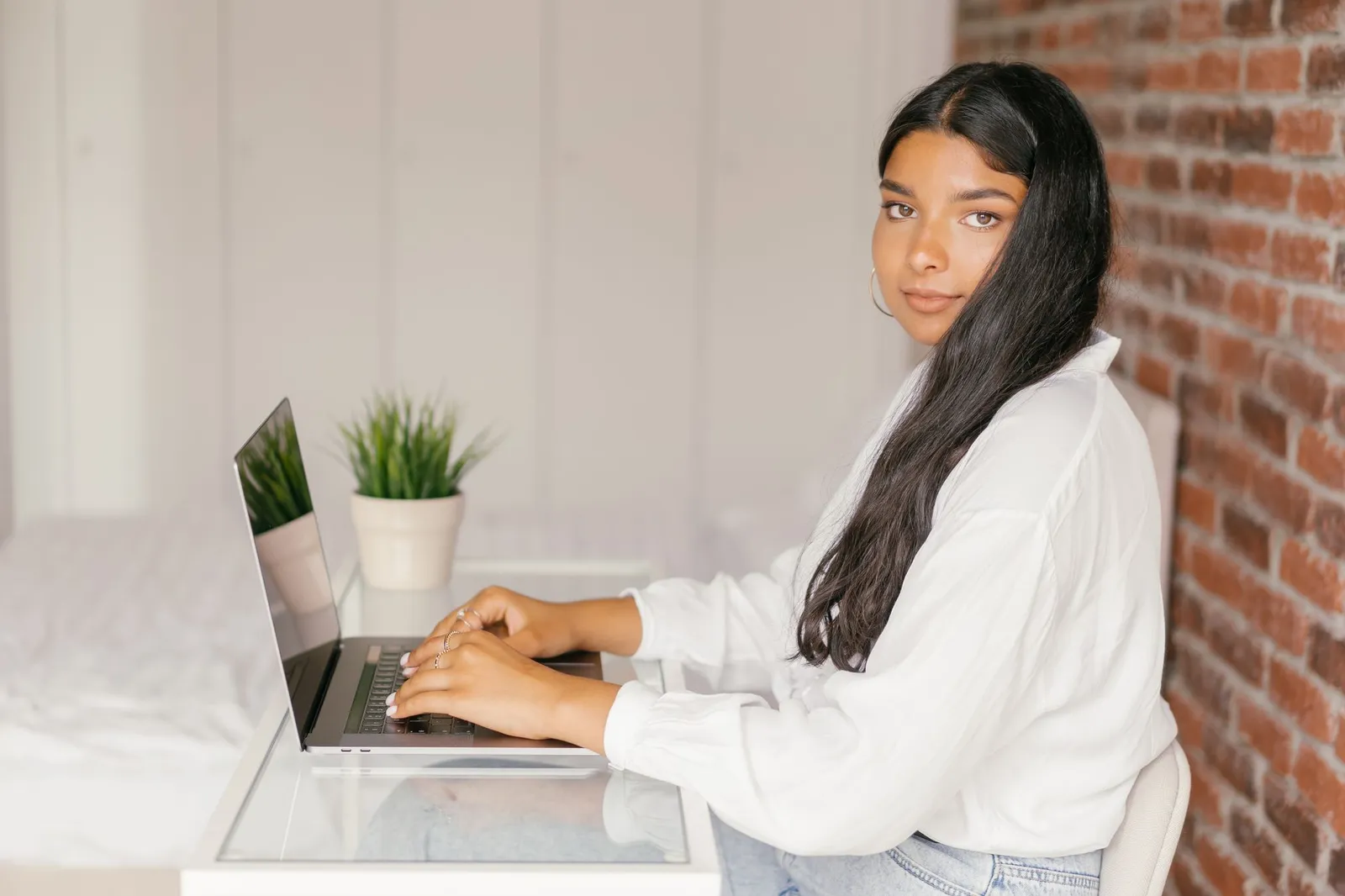Young woman typing on a laptop beside a plant, studying for the AI-900 exam