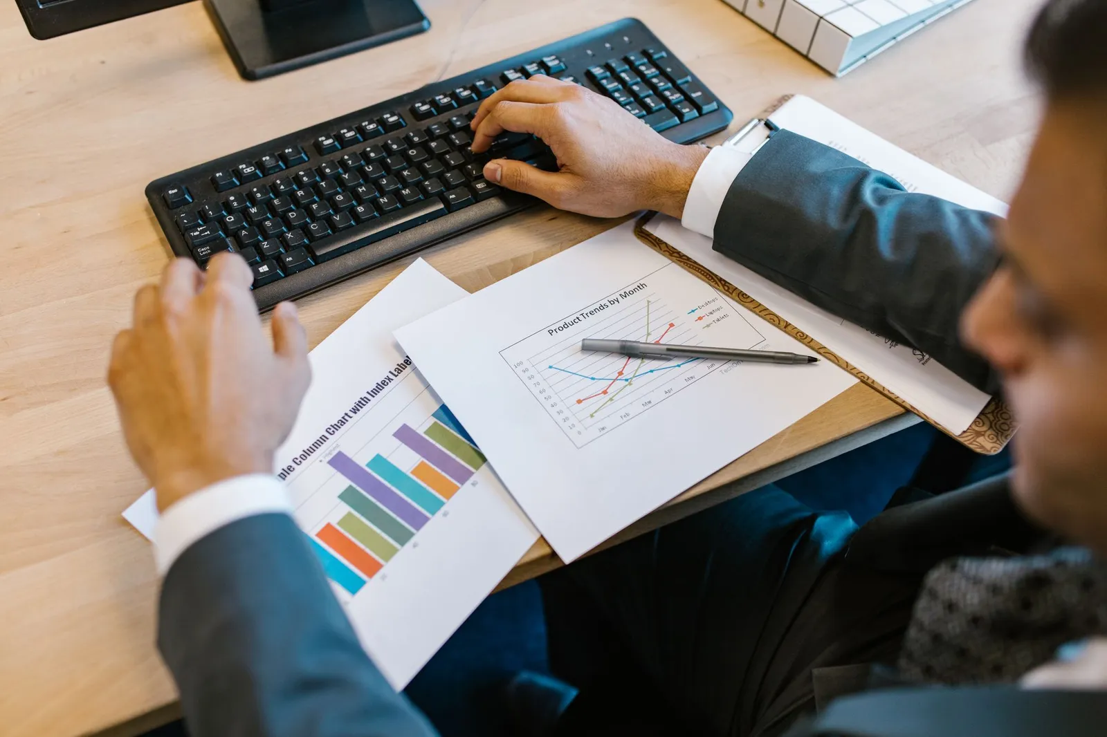 Man in a suit typing beside printed column and line charts, studying for the DP-100 data scientist exam