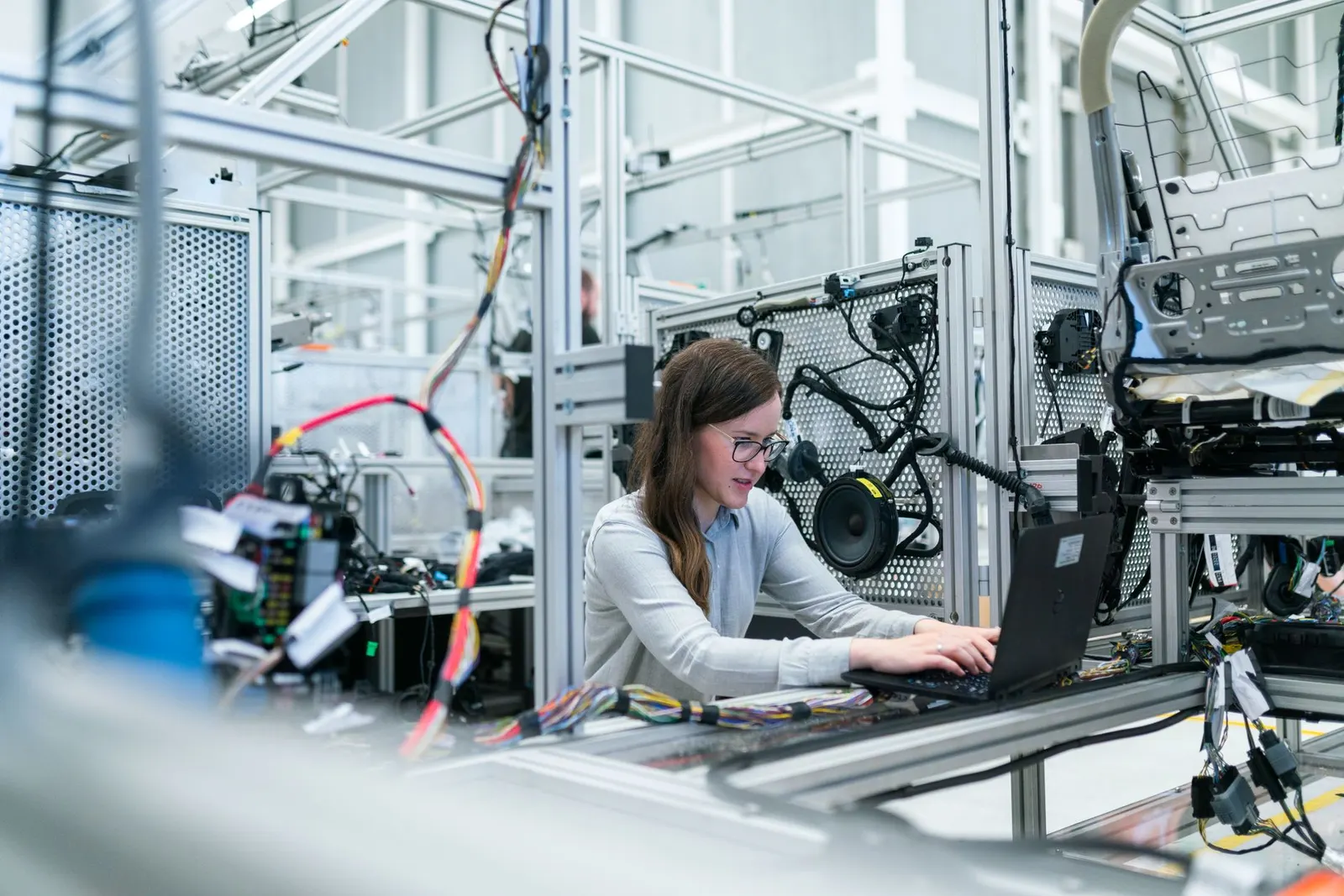 Robotics engineer typing on a laptop beside a test rig crowded with colored wiring