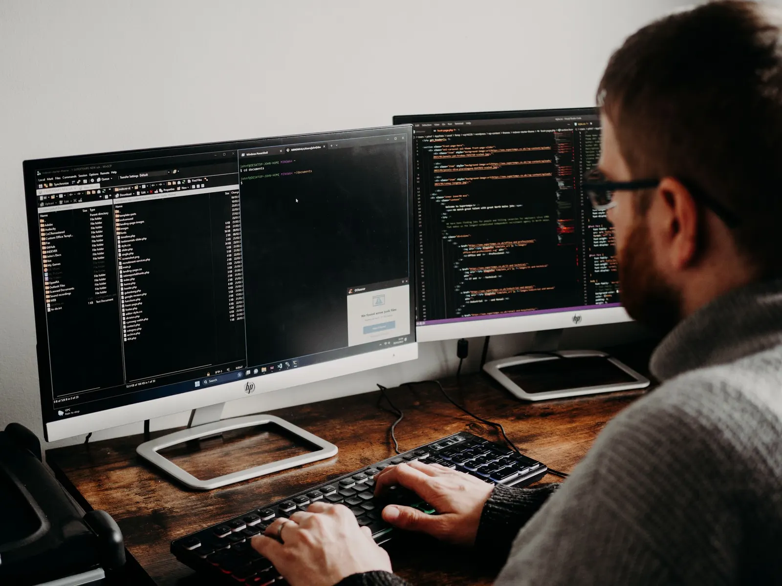 Software engineer typing at a wooden desk with two monitors of code